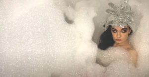 Kristeen Young - The Beauty Shop promo video thumbnail. Image from the video of Kristeen Young in a bath full of a huge mound of bubbles.